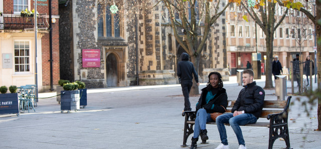 两个学生坐在长凳上聊天。在他们后面是雷丁镇中心的一座老教堂。