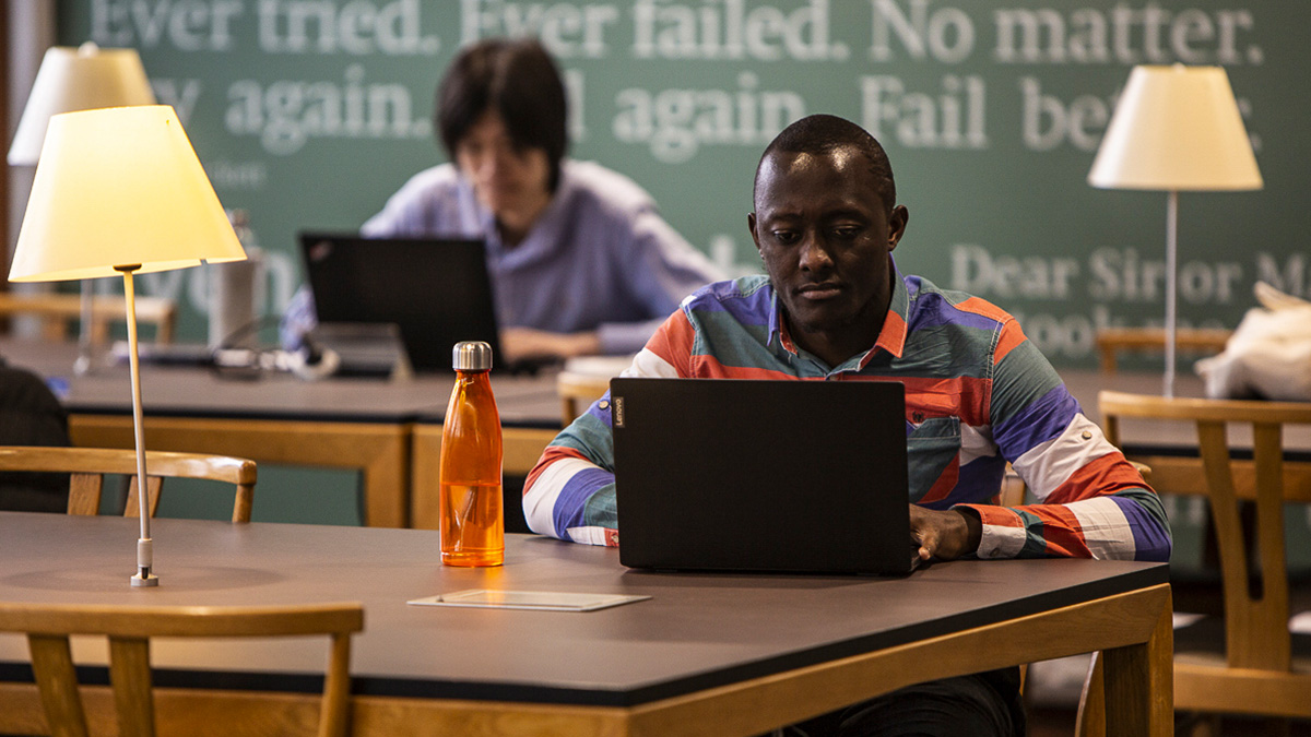 男学生坐在图书馆的桌子上用笔记本电脑学习